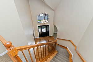 Foyer entrance featuring a chandelier, high vaulted ceiling, wood finished floors, arched walkways, and stairway