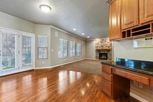 Kitchen featuring brown cabinets, open floor plan, dark wood-style floors, a textured ceiling, and a stone fireplace