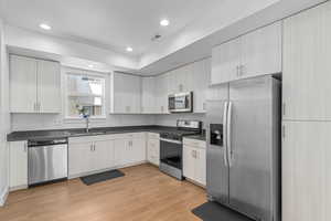 Kitchen featuring stainless steel appliances, light wood-style floors, dark countertops, recessed lighting, and white cabinetry