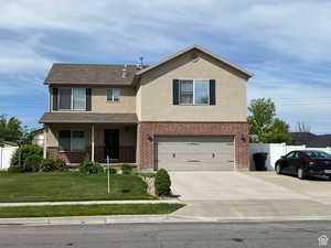 Traditional-style house with covered porch, stucco siding, concrete driveway, an attached garage, and brick siding