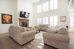 Living area with healthy amount of natural light, wood finished floors, a stone fireplace, and a towering ceiling