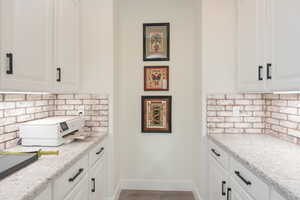 Kitchen with tasteful backsplash, white cabinetry, light stone counters, and light wood-style flooring