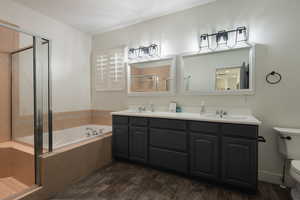 Bathroom with a stall shower, a bath, double vanity, and dark wood finished floors