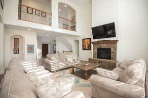 Living area featuring arched walkways, wood finished floors, a stone fireplace, a towering ceiling, and recessed lighting