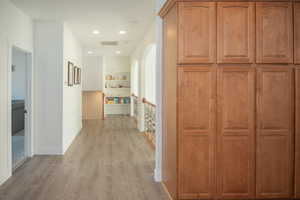 Hall featuring light wood finished floors, recessed lighting, an upstairs landing, and arched walkways