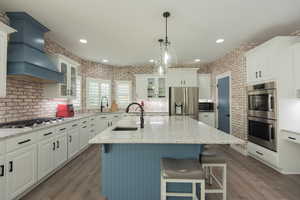 Kitchen with a center island with sink, appliances with stainless steel finishes, glass insert cabinets, light stone countertops, and blue cabinetry
