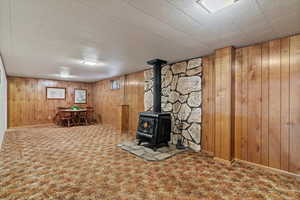 Finished below grade area featuring a wood stove, carpet flooring, and wood walls