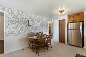 Dining area featuring light colored carpet, wallpapered walls, and a wainscoted wall