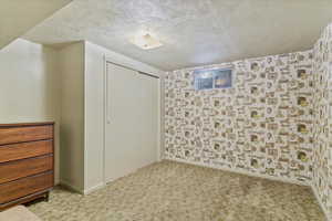 Unfurnished bedroom featuring a textured ceiling, a closet, and light carpet
