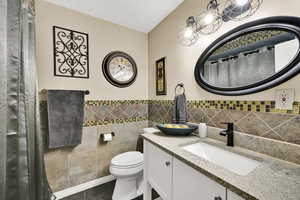 Bathroom featuring tile walls, vanity, dark tile patterned flooring, a shower with shower curtain, and a wainscoted wall