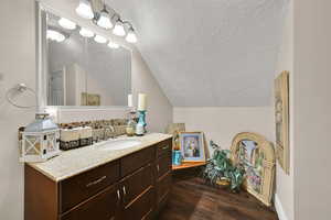 Bathroom featuring a textured ceiling, lofted ceiling, dark wood-style flooring, and vanity