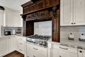 Kitchen with tasteful backsplash, light stone counters, custom range hood, stainless steel gas stovetop, and white cabinets