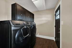Washroom featuring dark wood finished floors, cabinet space, and washer and clothes dryer