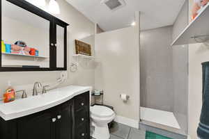 Full bath featuring light tile patterned floors, a walk in shower, vanity, and a textured ceiling