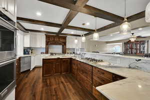 Kitchen with pendant lighting, stainless steel appliances, dark wood-type flooring, decorative backsplash, and light stone countertops