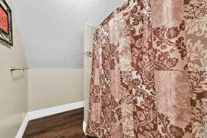 Bathroom featuring a textured ceiling, dark wood-style flooring, vaulted ceiling, and curtained shower