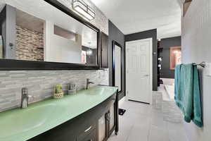 Bathroom featuring a textured ceiling, light tile patterned floors, double vanity, and backsplash