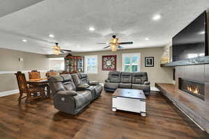 Living room with a tile fireplace, a textured ceiling, dark wood-style floors, ceiling fan, and recessed lighting