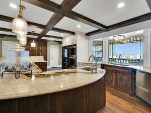 Kitchen featuring dark wood-style floors, pendant lighting, beam ceiling, light stone countertops, and coffered ceiling