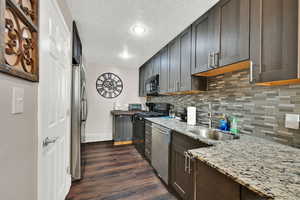 Kitchen with backsplash, light stone countertops, a textured ceiling, black appliances, and dark wood finished floors
