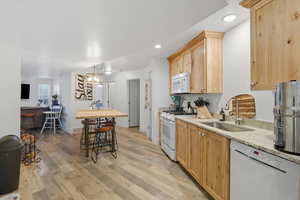 Kitchen 3 with white appliances, light brown cabinets, light wood finished floors, light stone countertops, and hanging light fixtures