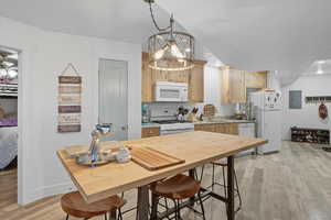 Kitchen 3 with light wood-style floors, light brown cabinetry, white appliances, hanging light fixtures, and electric panel