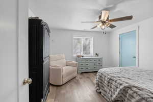 Bedroom with light wood-style floors, ceiling fan, and a textured ceiling