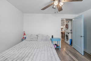 Bedroom with wood finished floors, stacked washer / drying machine, and ceiling fan