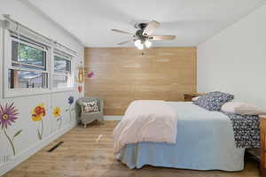 Bedroom featuring wooden walls, wood finished floors, an accent wall, and ceiling fan