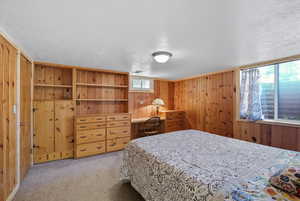 Carpeted bedroom featuring wooden walls, a textured ceiling, and a closet