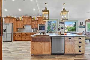 Kitchen 1 featuring stainless steel appliances, a center island with sink, pendant lighting, light stone counters, and decorative backsplash