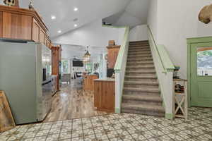 Kitchen with stainless steel fridge, high vaulted ceiling, brown cabinets, recessed lighting, and pendant lighting