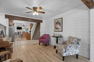 Sitting room featuring light wood finished floors, stairway, wood walls, ceiling fan, and a textured ceiling