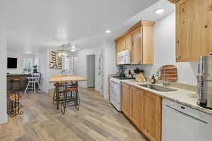 Kitchen 3 featuring white appliances, light wood-type flooring, decorative light fixtures, light stone countertops, and light brown cabinetry