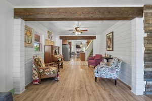 Sitting room featuring light wood finished floors, wood walls, a ceiling fan, beamed ceiling, and stairs