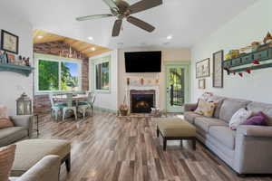 Living area featuring vaulted ceiling, wood finished floors, a brick fireplace, brick wall, and ceiling fan