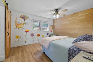 Bedroom with wood finished floors, wooden walls, a barn door, and ceiling fan