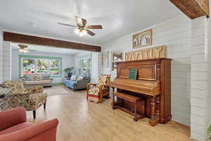 Living area featuring light wood-type flooring, a textured ceiling, wood walls, healthy amount of natural light, and ceiling fan