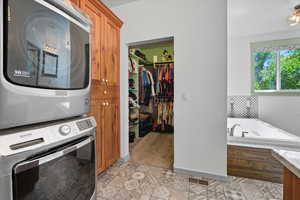 Laundry area with stacked washer and clothes dryer and light tile patterned flooring