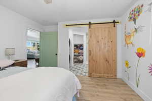 Bedroom with light wood-style flooring, a ceiling fan, and a barn door