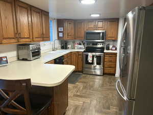 Kitchen with appliances with stainless steel finishes, a peninsula, light countertops, and brown cabinetry