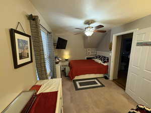 Bedroom with vaulted ceiling, light colored carpet, a textured ceiling, and a ceiling fan