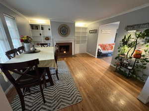 Dining area with a fireplace, wood finished floors, ornamental molding, and built in shelves
