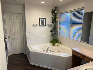 Bathroom with a jetted tub, dark wood-style flooring, recessed lighting, and vanity