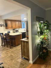 Kitchen featuring brown cabinets, light countertops, a breakfast bar, dishwasher, and ornamental molding