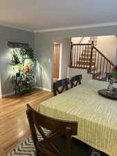 Dining space with ornamental molding, light wood-style floors, and stairs