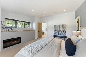 Carpeted bedroom featuring a glass covered fireplace, recessed lighting, and connected bathroom