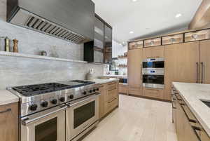 Kitchen with open shelves, premium range hood, appliances with stainless steel finishes, modern cabinets, and light stone counters