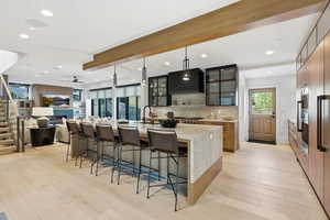 Kitchen featuring glass insert cabinets, a spacious island, a kitchen breakfast bar, light stone countertops, and decorative light fixtures