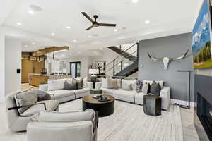 Living area featuring stairs, ceiling fan, a glass covered fireplace, recessed lighting, and light wood-style floors